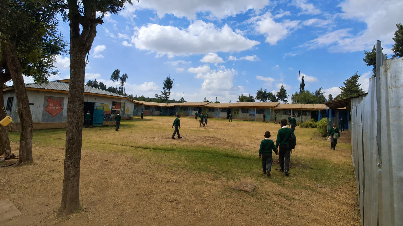 A wide view of learners, trees, and classroom blocks at Betha Academy